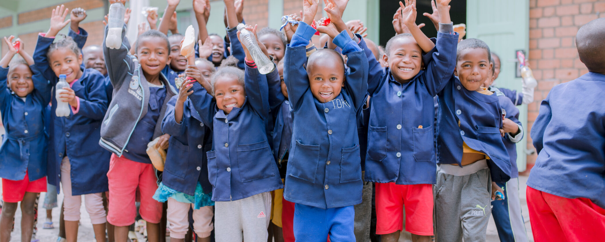 Group of children smiling at the camera, holding up their hands and arms in the air.