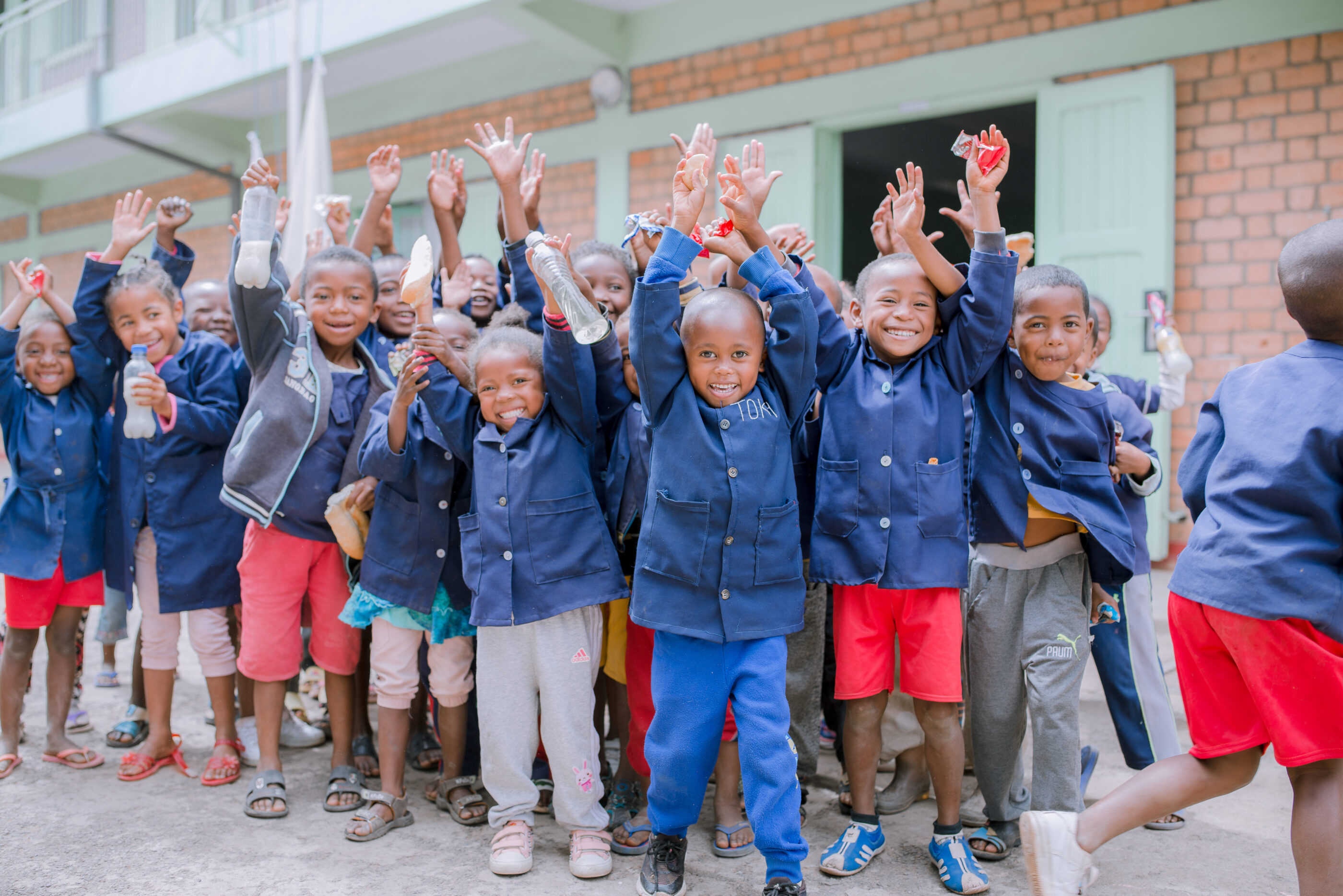 Group of children smiling at the camera, holding up their hands and arms in the air.