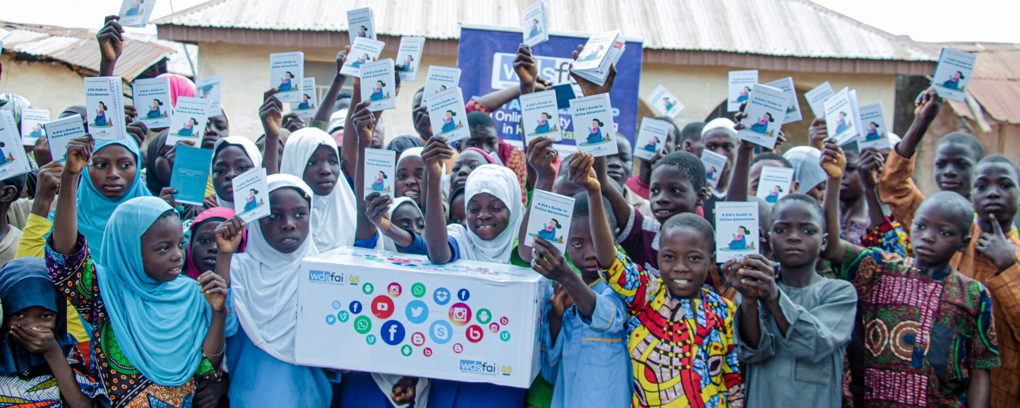 A diverse group of children in hijabs proudly holds tcards after completing a digital safeguarding course.