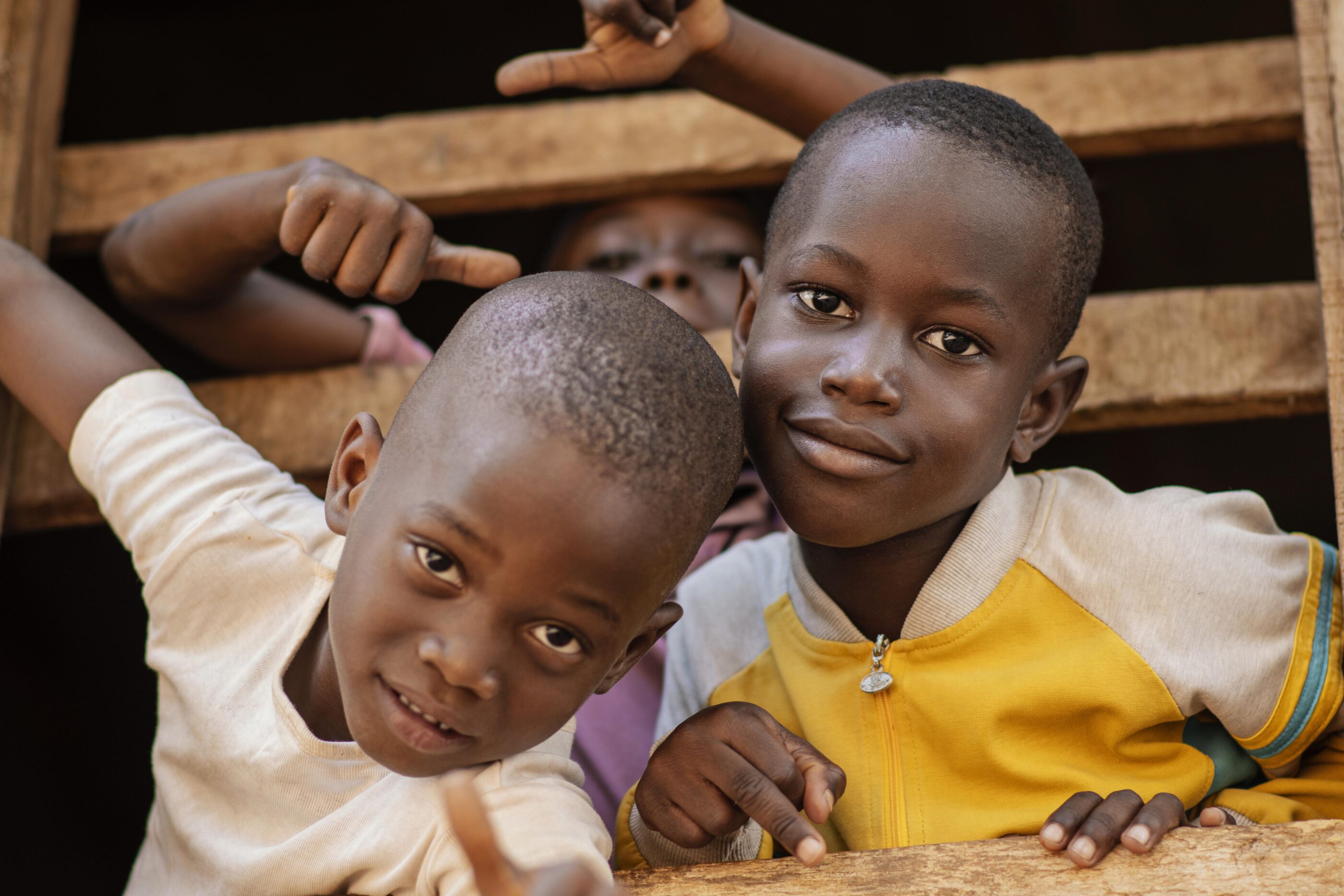 Two young boys stand together inside a wooden structure, smiling.